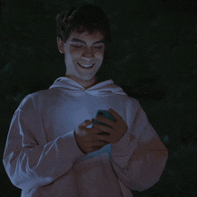 a young man wearing a white hoodie with a green circle on the front smiles