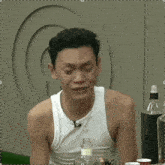 a man in a white tank top is sitting in front of a wall