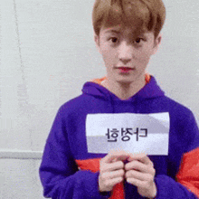 a young man in a purple hoodie is holding a piece of paper that says ' a ' on it .