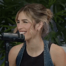 a woman is smiling in front of a microphone while wearing a denim vest .
