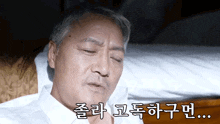 a man in a white shirt is laying on a bed with his eyes closed and a caption in korean