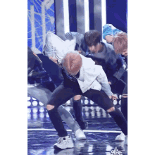 a group of young men are dancing on a stage and one of them is wearing a white shirt