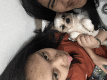 two girls laying on a bed with a small white dog