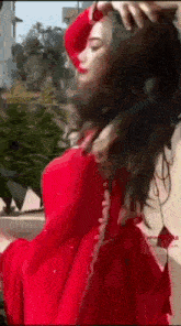a woman in a red dress is standing in front of a building with her hair blowing in the wind .