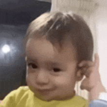a baby is holding his hand to his ear while making a funny face .