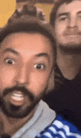 a man with a beard is making a funny face while taking a selfie with two other men .