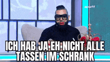 a man with a beard and sunglasses is sitting on a couch with a crown on his head .