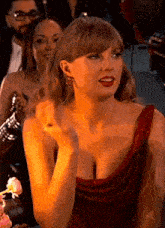 taylor swift is wearing a red dress and red lipstick while sitting in a crowd of people .