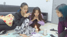 a group of girls sitting around a cake with candles