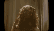 a woman with long curly hair is standing in front of a window in a room .