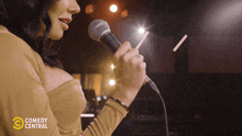 a woman singing into a microphone with a comedy central logo behind her