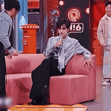 a man is sitting on a pink couch holding a microphone and talking to a woman .