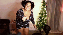 a woman wearing headphones and a sweater is dancing in front of a christmas tree