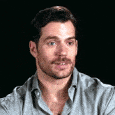 a man with a beard and mustache is wearing a gray shirt and smiling .