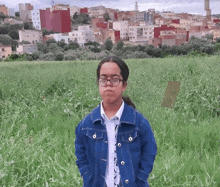 a girl with glasses and a blue jacket stands in a field