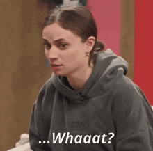 a woman wearing a grey hoodie is making a funny face and says whaaat ?