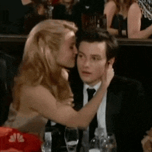 a woman is kissing a man on the cheek in a crowd of people .