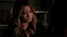 a woman in a black jacket is sitting in a dark room looking at another woman .