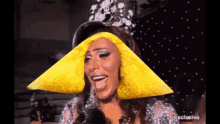 a woman wearing a crown with a yellow cone on her head is talking into a microphone with the words exclusive behind her