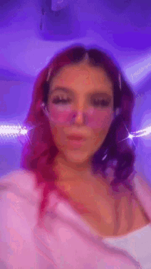a woman with pink hair and pink glasses is standing in front of a purple light .