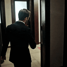 a man in a black suit is walking through a hallway