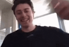 a man in a black shirt is smiling while holding a glass of water .