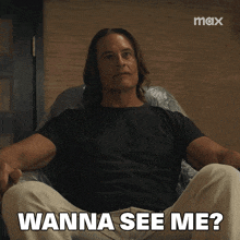 a man in a black shirt is sitting in a chair and says wanna see me