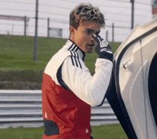 a man wearing a red and white adidas jacket holds his nose