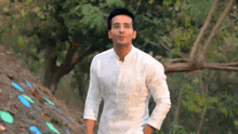 a man in a white shirt is standing in front of a tree .