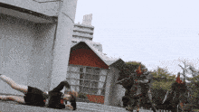 a person is laying on the ground in front of a building while a group of monsters are standing behind them .