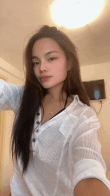 a woman in a white shirt is taking a selfie in front of a television