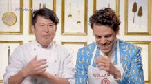 a man wearing an apron that says avellana laughs with another man