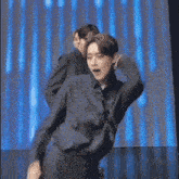 a man in a black shirt is dancing on a stage in front of a blue light .