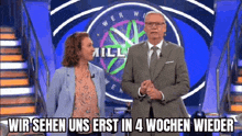 a man and a woman are standing on a stage in front of a wheel of fortune sign .