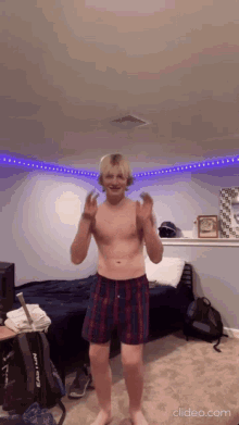 a shirtless man in plaid boxers is dancing in a bedroom with a backpack that says easton on it
