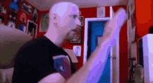 a bald man in a black shirt is standing in a room with a purple light behind him .