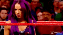a woman with purple hair is standing in a wrestling ring with a crowd behind her .