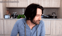 a man in a blue sweatshirt is sitting in a kitchen with his eyes closed and the hashtag @itsscottiesstark above him