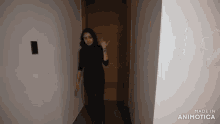 a woman in a black turtleneck and black pants is standing in a hallway and waving .