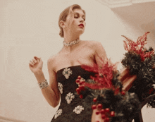 a woman in a black strapless dress is standing next to a christmas wreath