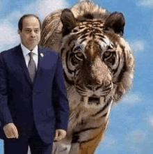 a man in a suit and tie is standing next to a tiger with its mouth open .