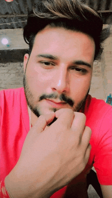a man with a beard wearing a red shirt holds his hand to his chin