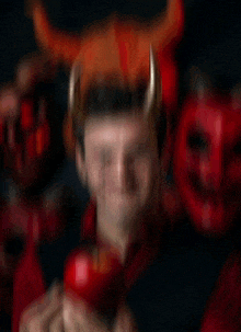 a man with horns is holding a red apple and the name eniko is on the bottom right
