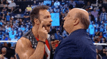 a wrestler is pointing at another wrestler 's face while talking into a microphone .