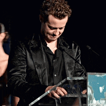 a man in a black jacket stands at a podium holding a plaque that says ' 2012 ' on it