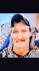 a man with long hair and a mustache is sitting in a chair .