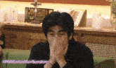 a man covering his mouth with his hands in front of a crucifix and a bible