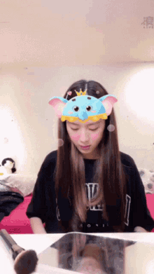 a girl wearing a blue elephant headband looks down at something