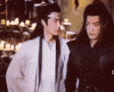 two men are standing next to each other and one has long black hair
