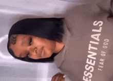 a woman wearing a hoodie with the word essentials on it is standing in front of a white curtain .